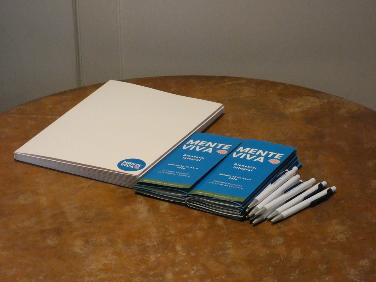 Materiales del encuentro de Mente Viva sobre una mesa: cuadernos, folletos de Bienestar Integral con la invitada especial Lic. Catalina Lamberti y lapiceras.