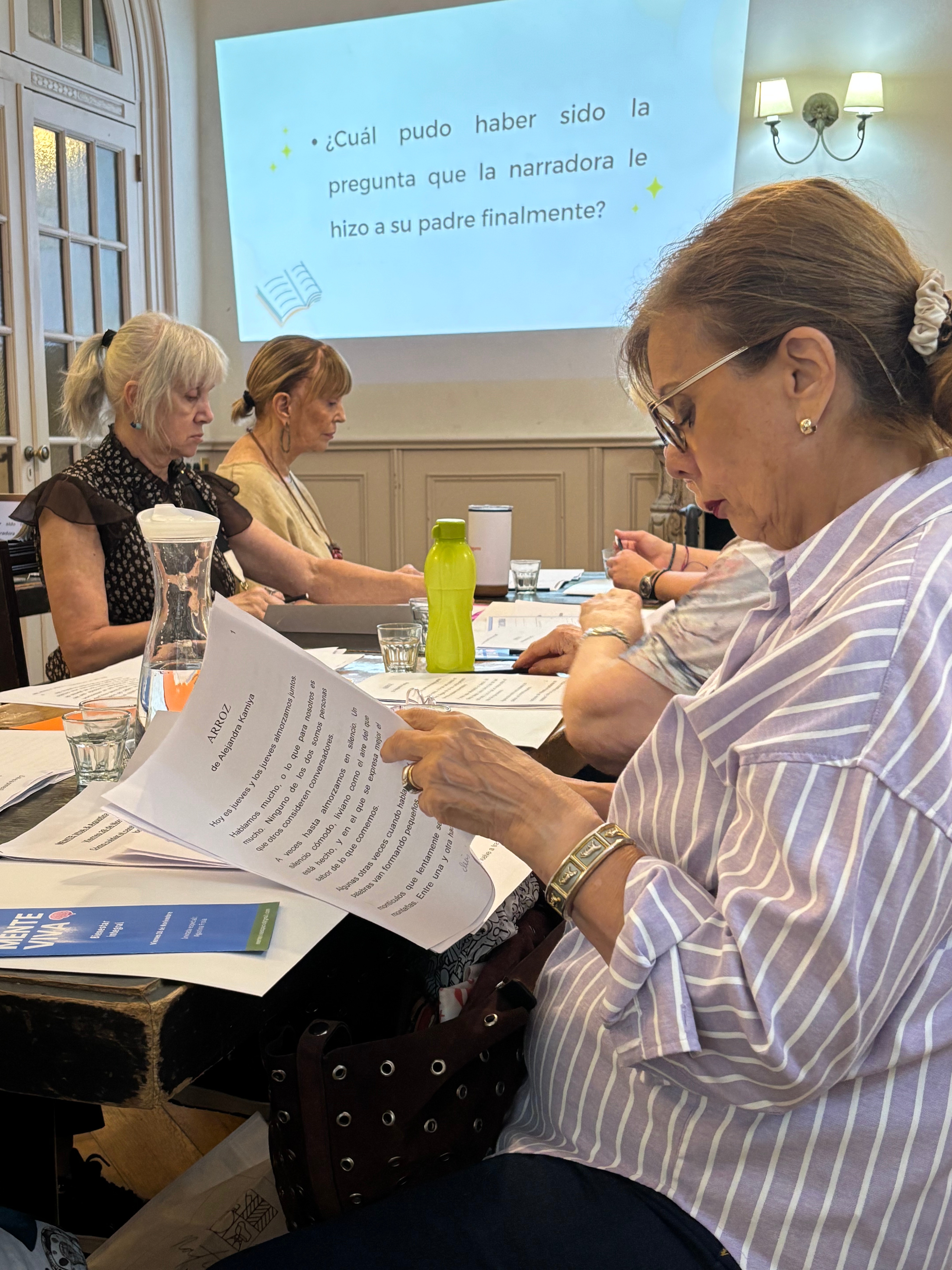 Una participante leyendo con atención el cuento 'Arroz' de Alejandra Kamiya, junto a otras lectoras y una diapositiva con una pregunta de comprensión proyectada.